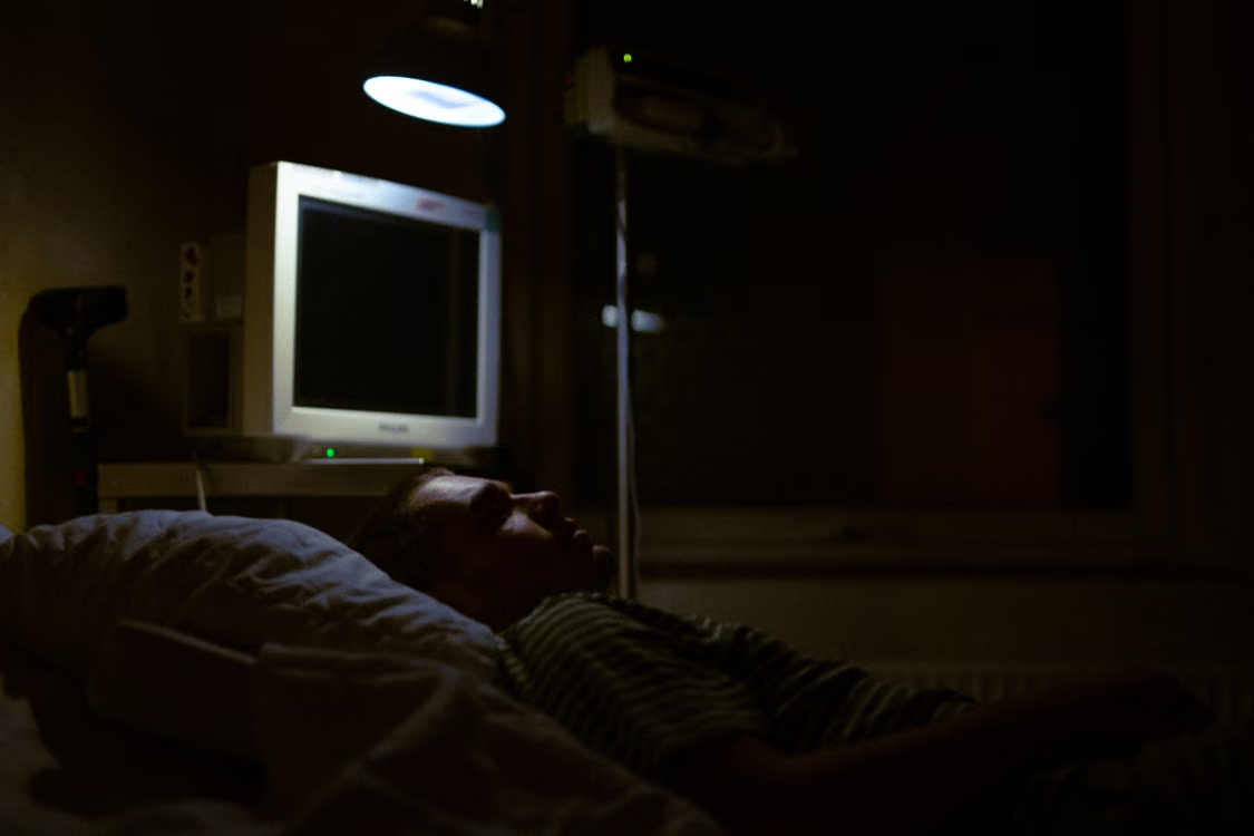 Patient resting beside powered medical equipment in a healthcare setting.